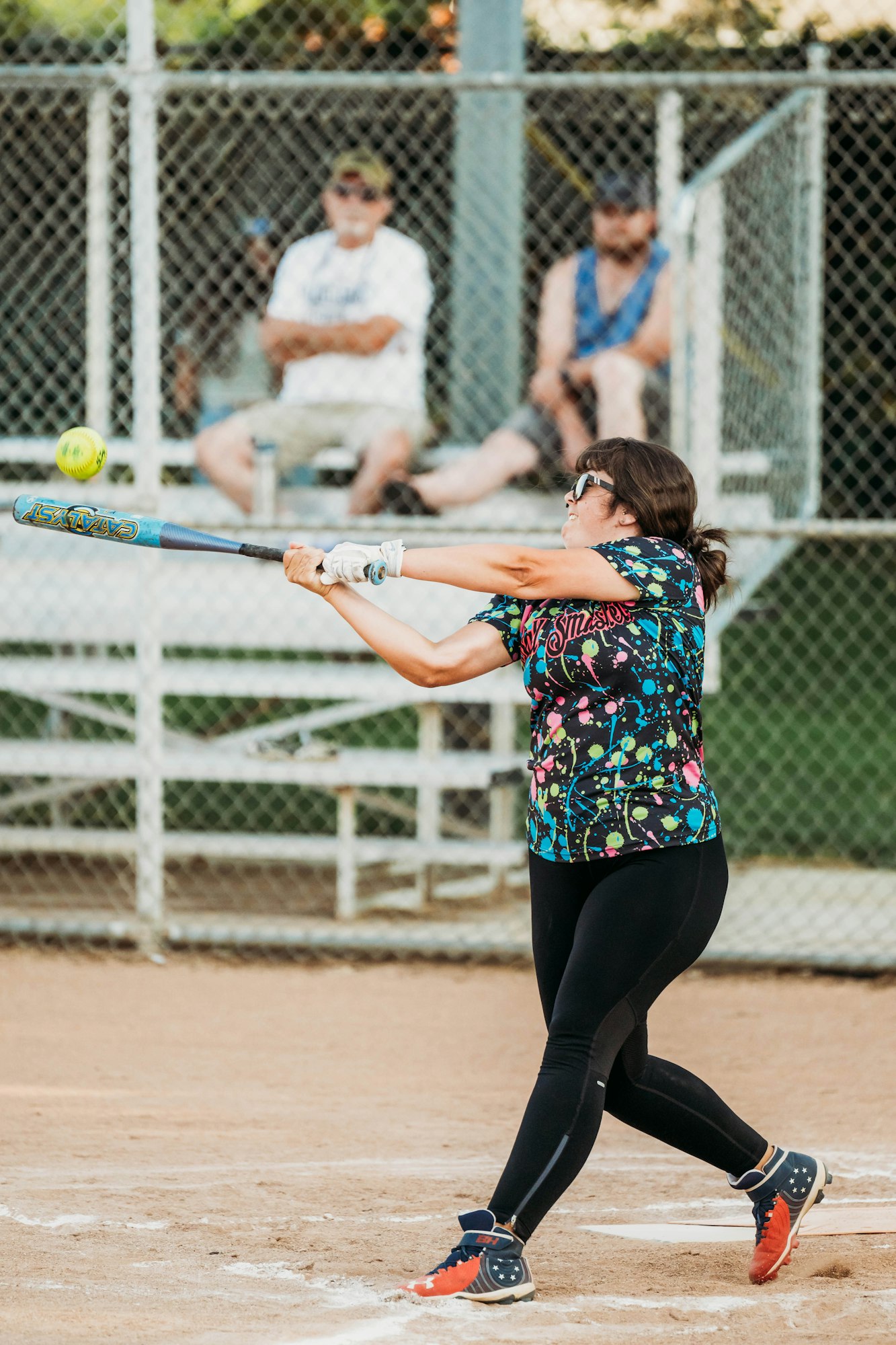 A softball player swinging at a pitch with spectators in the background.