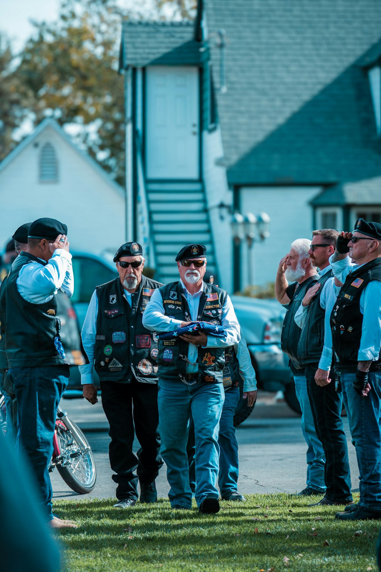A group of people in vests and berets, with some saluting while one holds a folded flag.