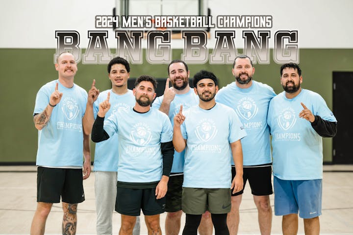 A men's basketball team celebrates their 2024 championship win, wearing matching blue "Champions" shirts.
