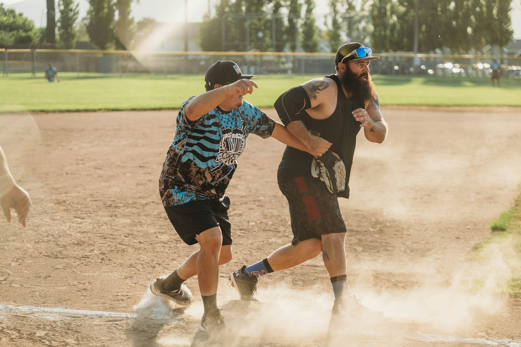 Two men playing softball, one running and another tagging, dust in the air.