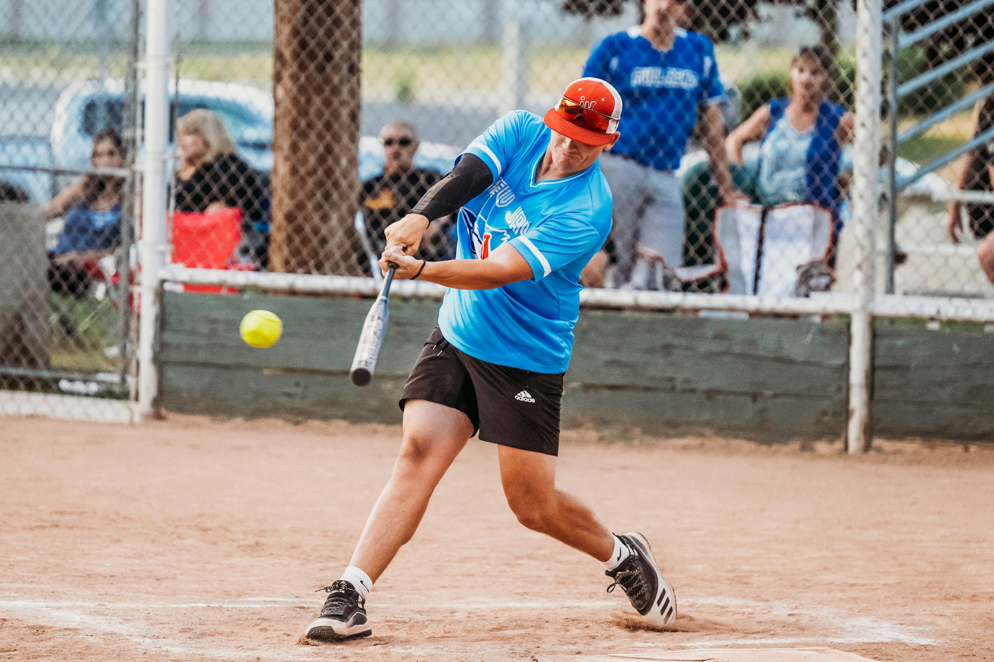 Person swinging bat at a softball game with spectators in the background.