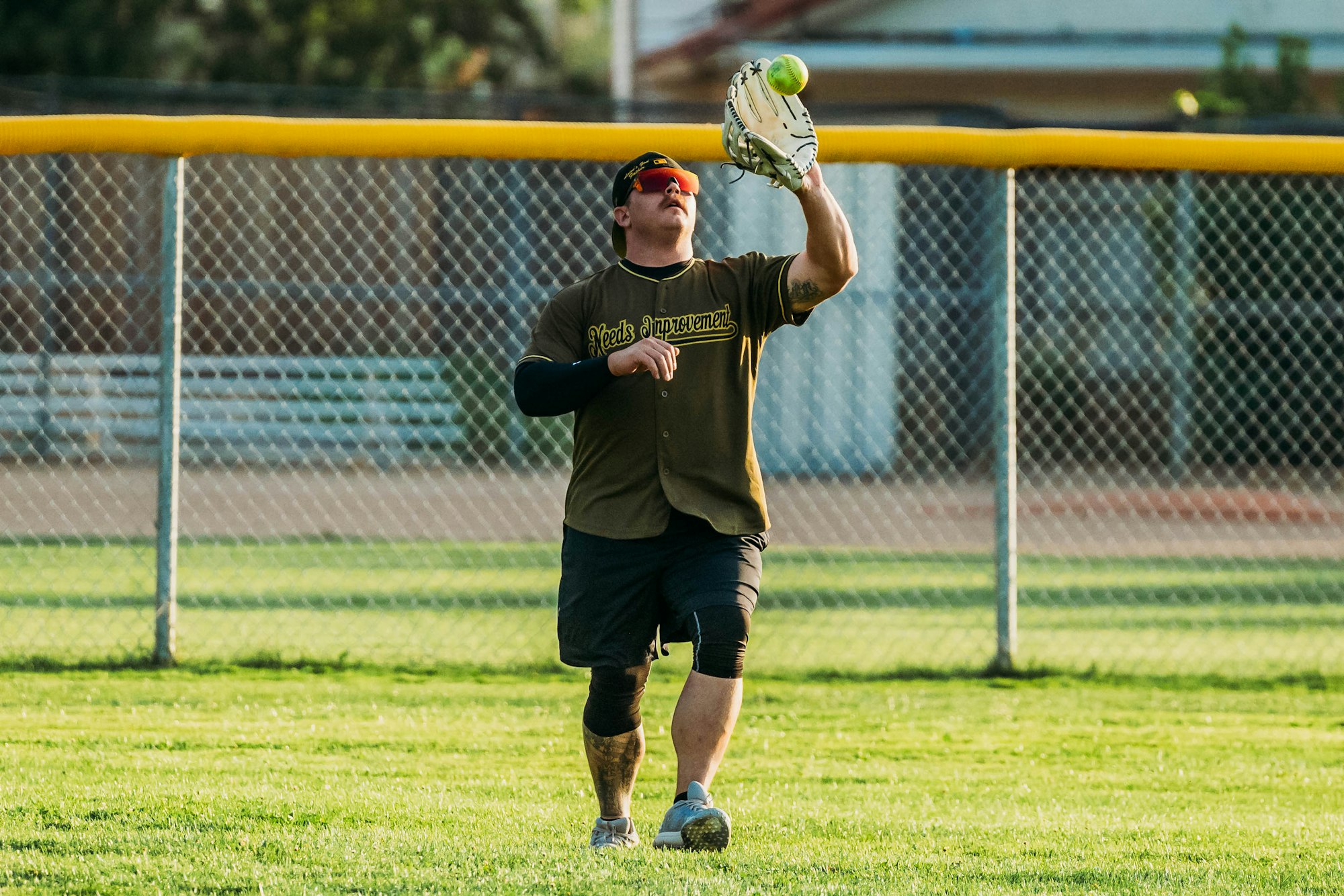 Person catching a softball on a field at dusk.