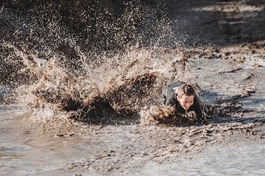 A person sliding through muddy water, creating a big splash.