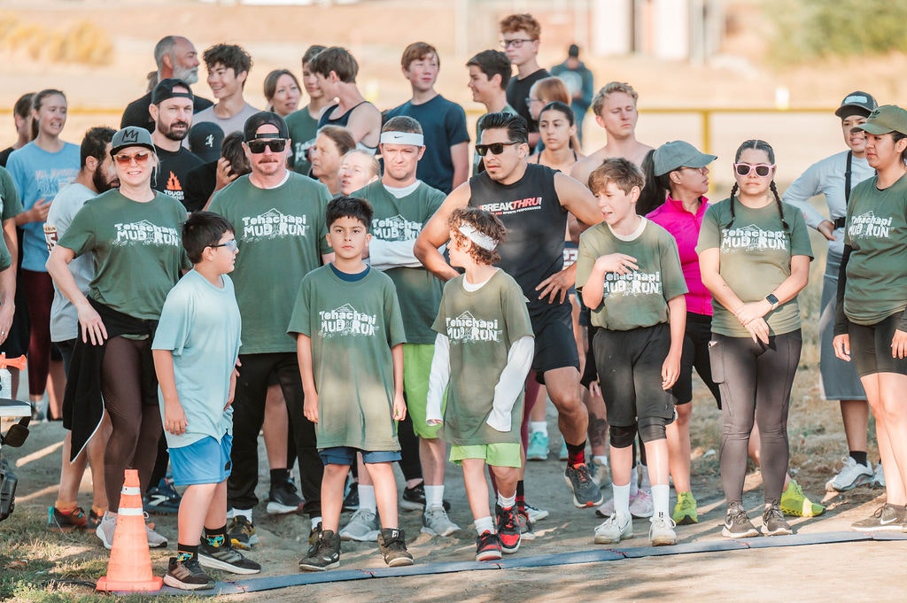 Group of people, including kids in green "Tehachapi Mud Run" shirts, at an outdoor event.