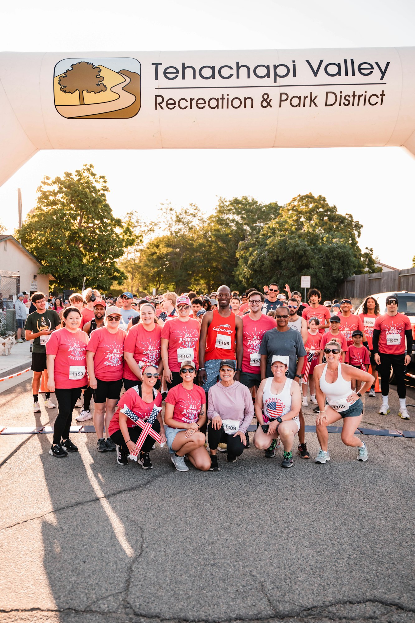 A group of people in athletic gear posing under a "Tehachapi Valley Recreation & Park District" banner, suggesting a race event.
