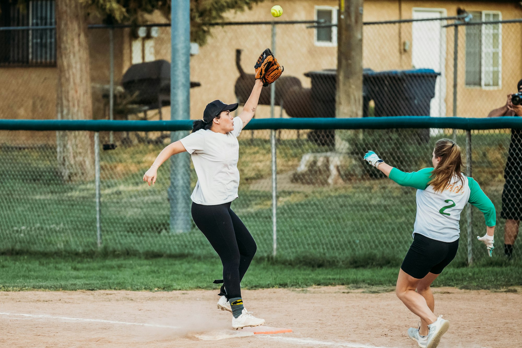 A softball game in action with a player catching a ball and another reaching base.