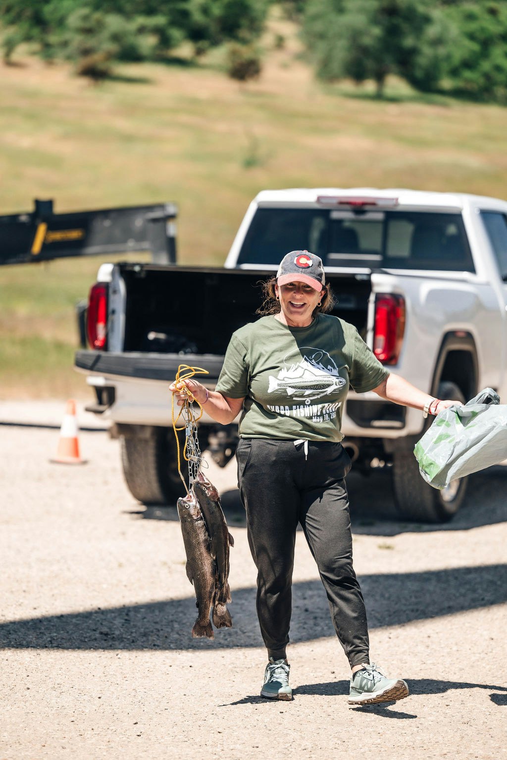 A person holding fish and a bag, smiling near a pickup truck.