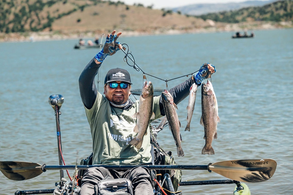 A person on a kayak holding up fish, with other boats in the background.