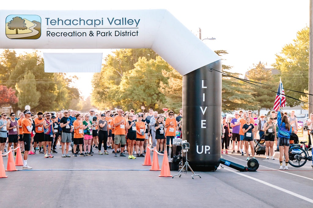A group of people stands at a race starting line under an inflatable arch that reads "Tehachapi Valley Recreation & Park District."