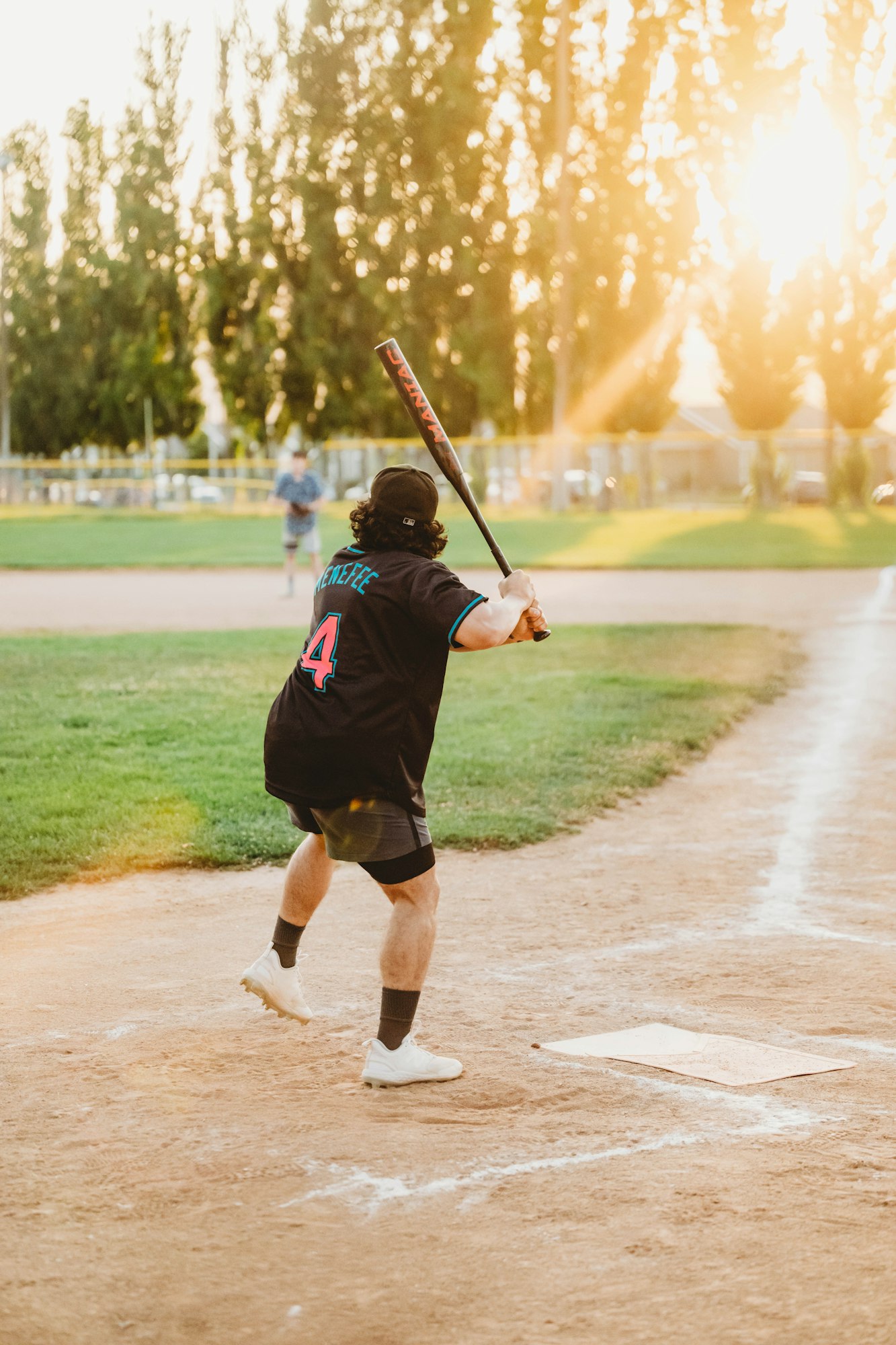 A player swinging a bat on a baseball field at sunset.