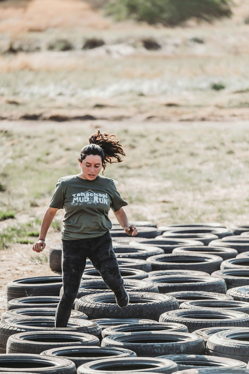 A person in a "Mud Run" shirt navigates a tire obstacle outdoors.