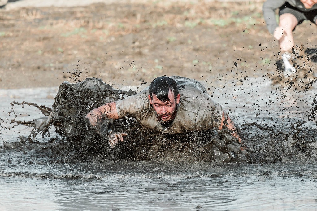 Person crawling through mud, splashing around during an obstacle race or mud run challenge.
