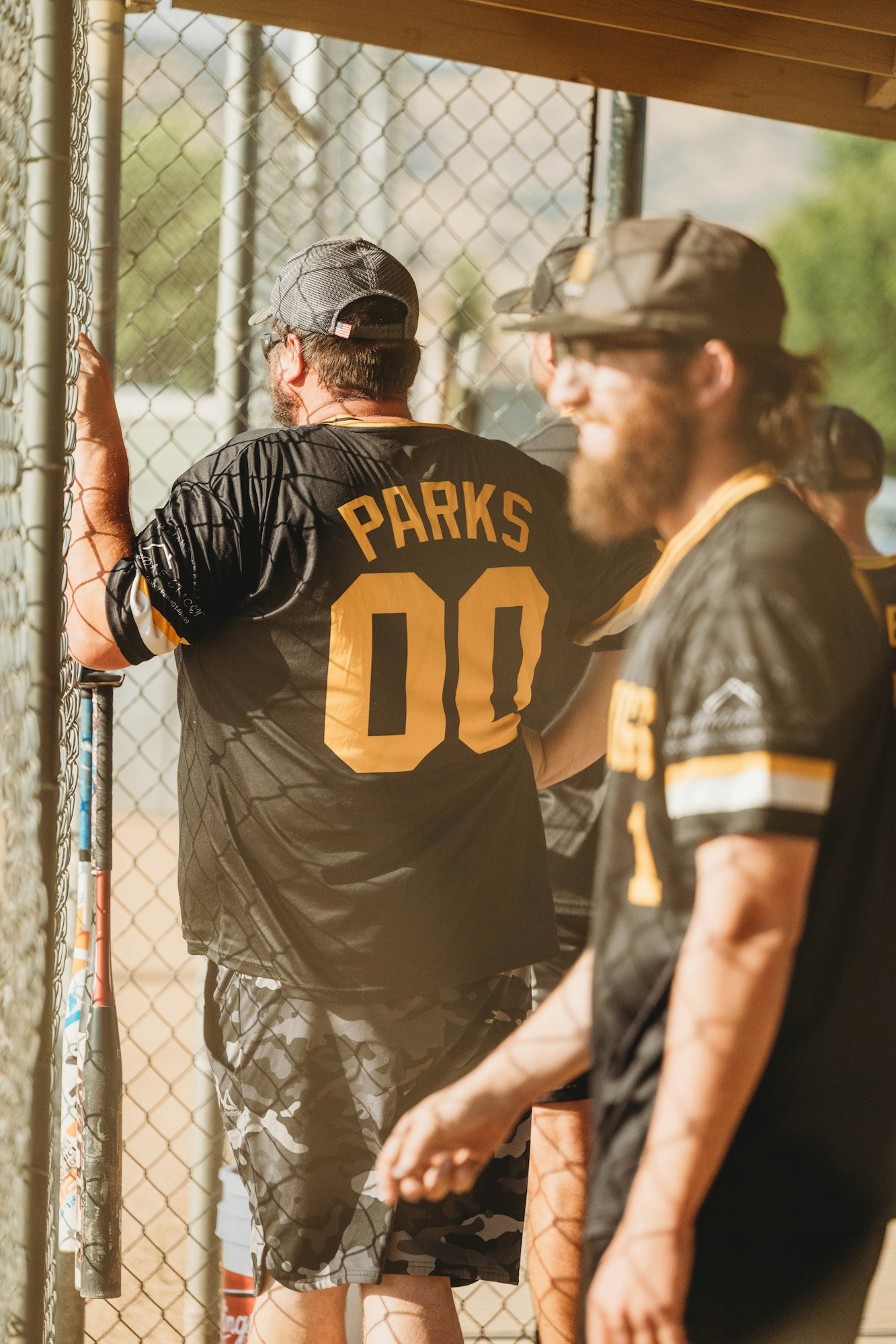 Two people in a dugout, one wearing a jersey with "PARKS 00," by a chain-link fence.