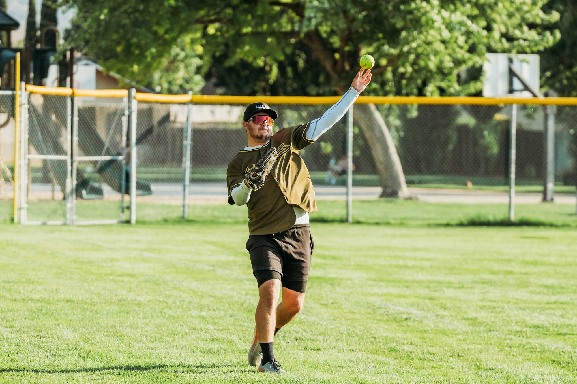 A man pitching a softball on a sunny field.