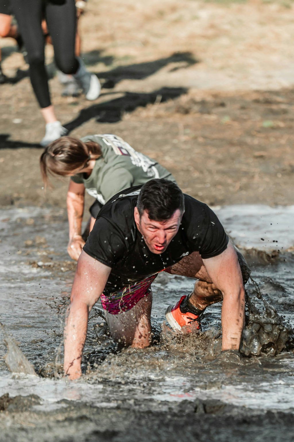 People crawling through muddy water during an outdoor obstacle race.