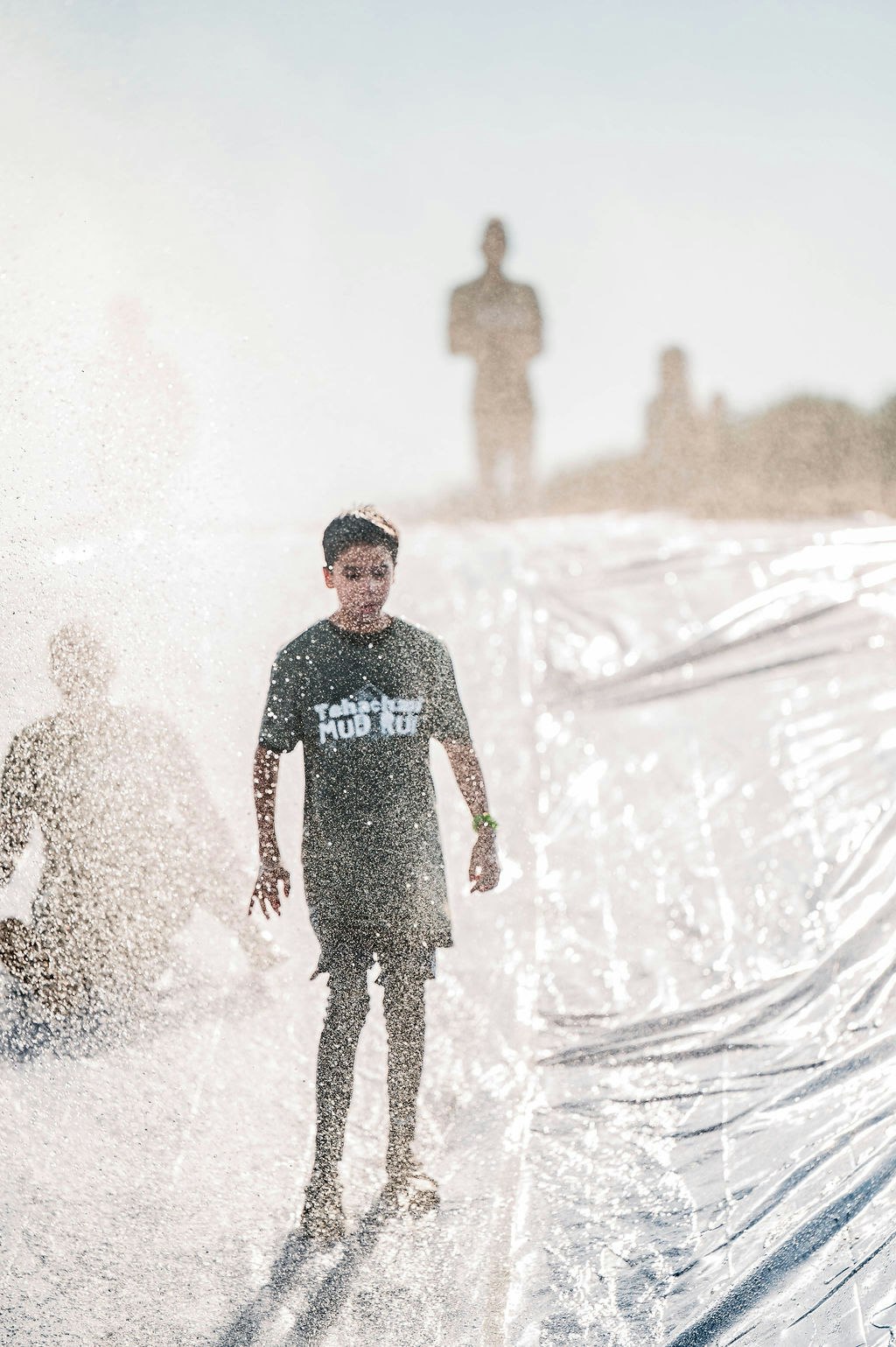 A person walking through water spray on a slippery surface, with blurred figures in the background.