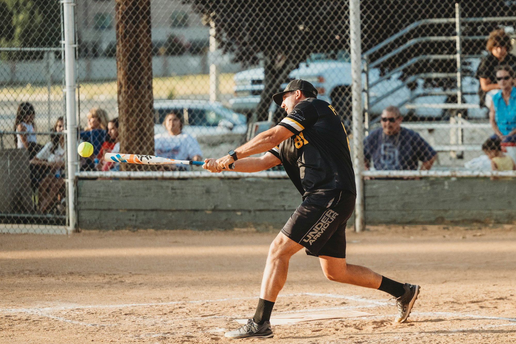 A player swinging at a softball in a dusty diamond, with spectators in the background.