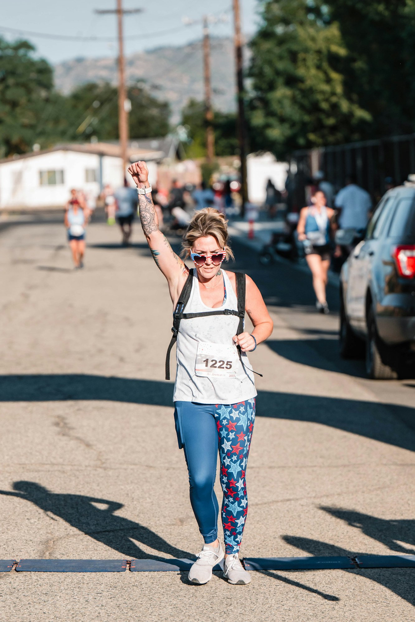 Runner finishing a race, wearing sunglasses and star-patterned leggings, with one arm raised triumphantly. 🏃♀️