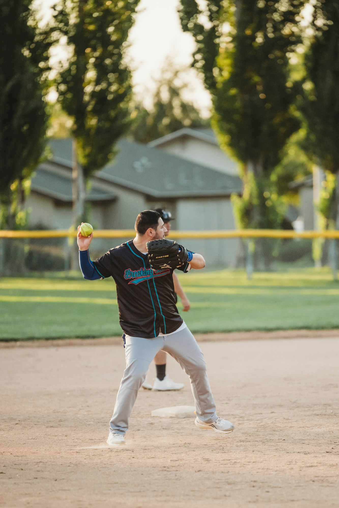 A person is pitching a softball on a sunny day at a park.