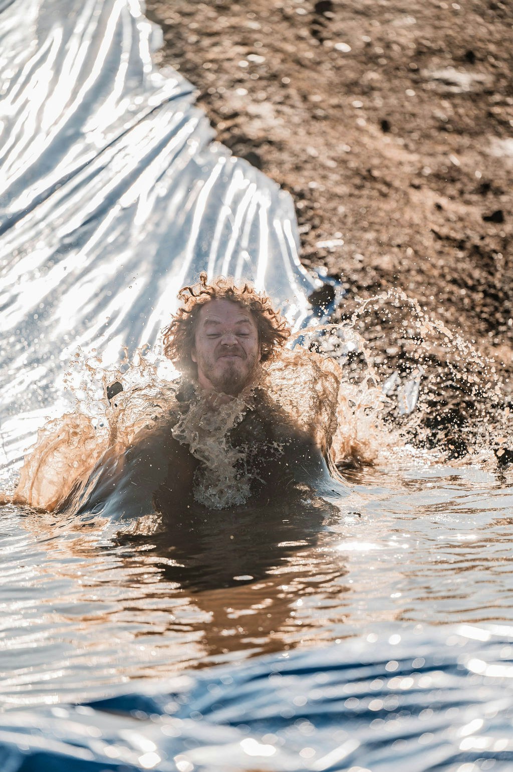 Person sliding into muddy water, creating a splash.