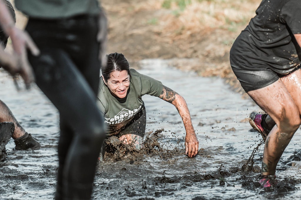 People crawling through muddy water during an outdoor event or obstacle course.