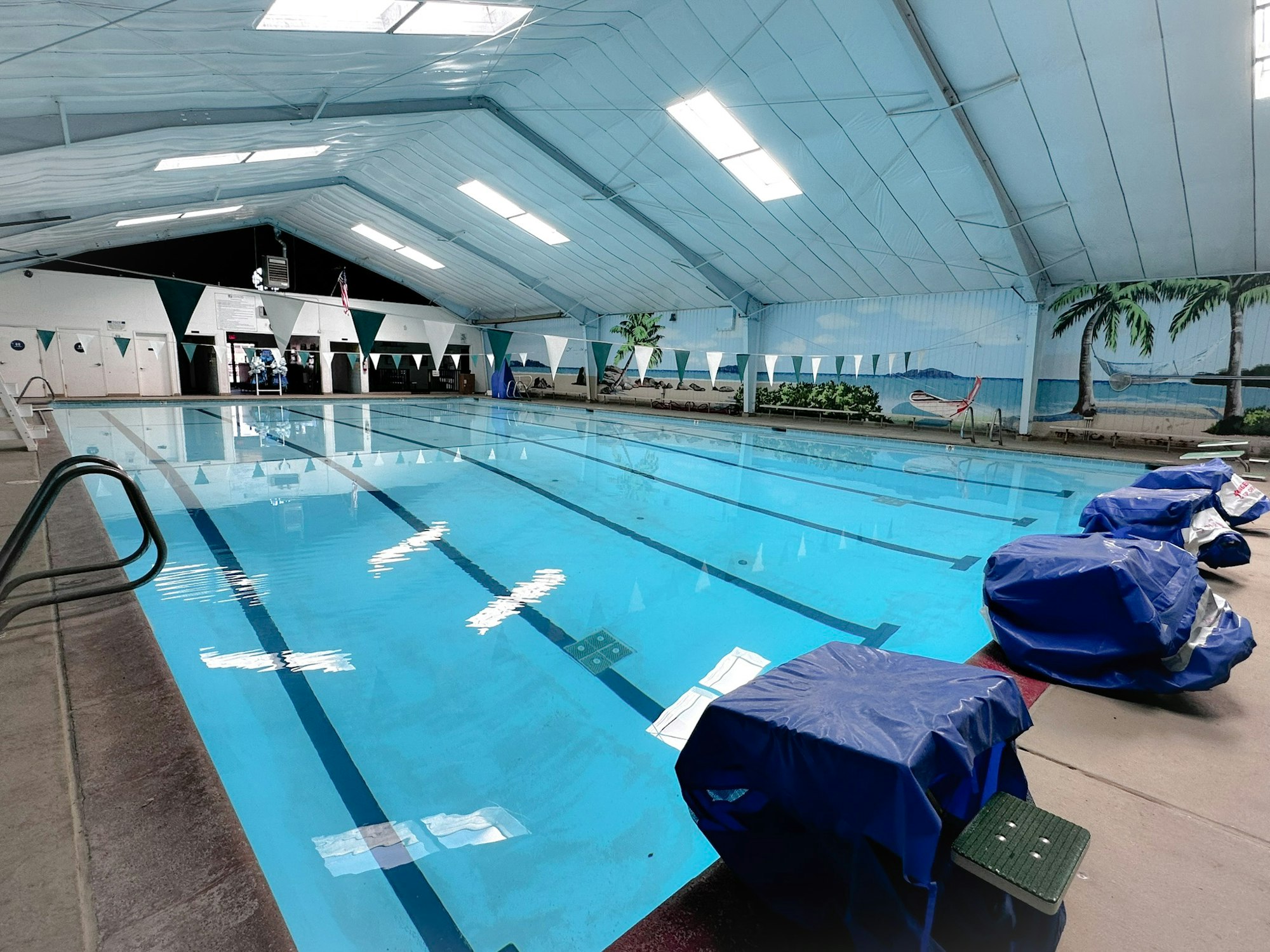 Indoor swimming pool with covered equipment and mural of a beach on the wall.