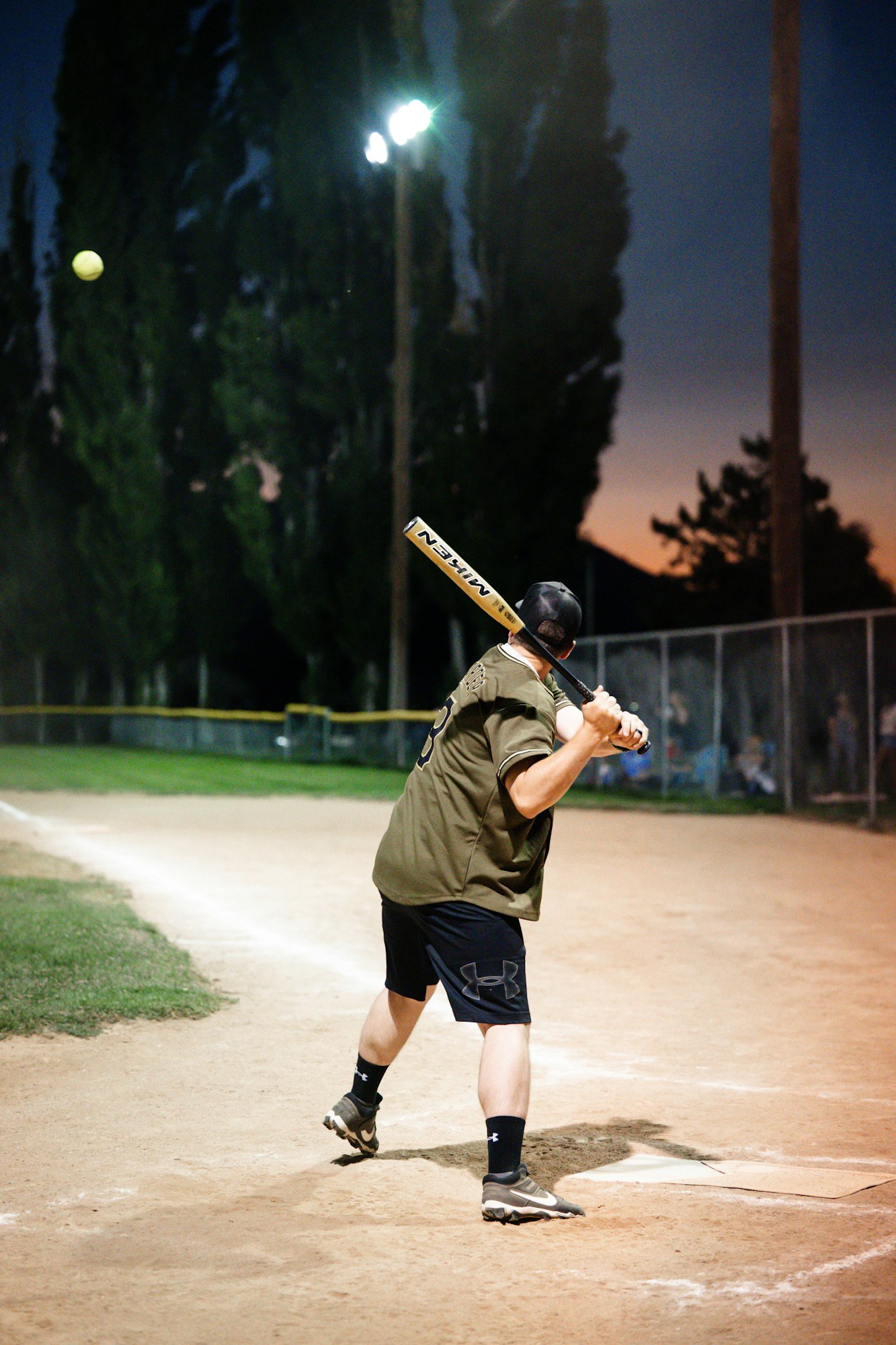 A batter in a night baseball game, preparing to hit an incoming pitch.