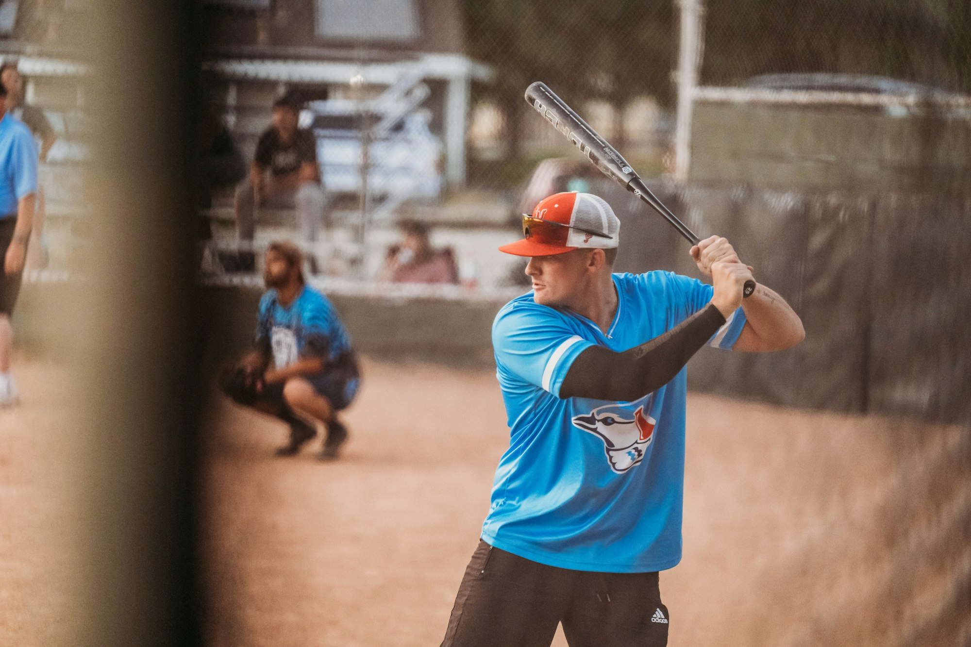 A baseball player ready to bat, with a catcher and umpire in the background, on a dusty field.