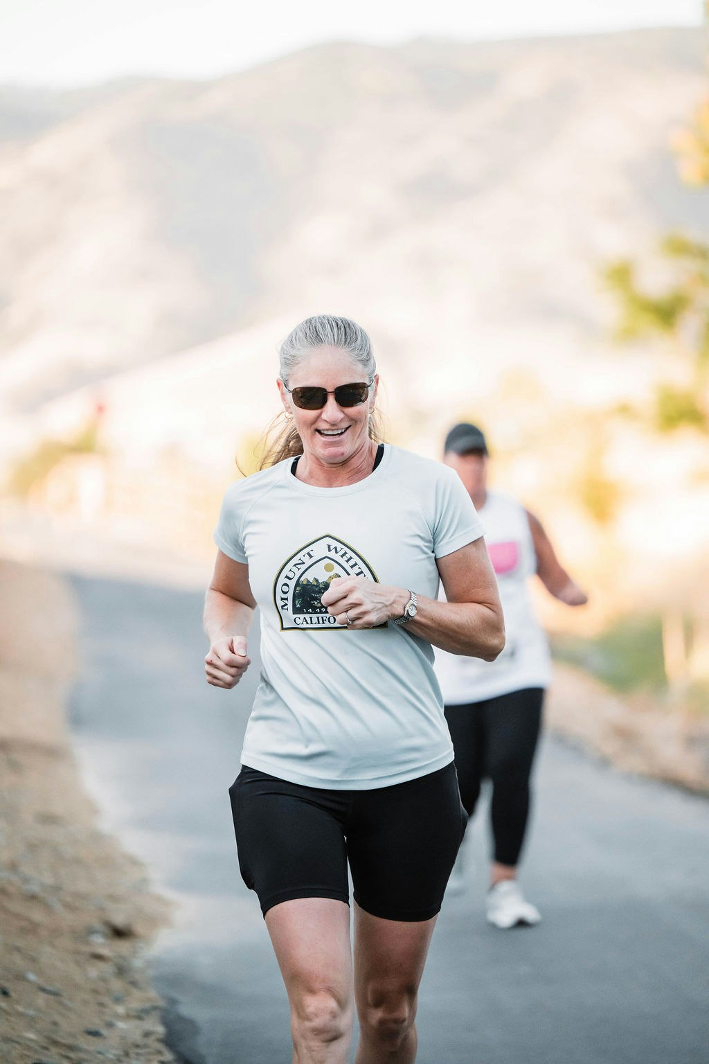 Two people running outdoors on a trail, one wearing sunglasses and a "Mount Whitney" T-shirt.