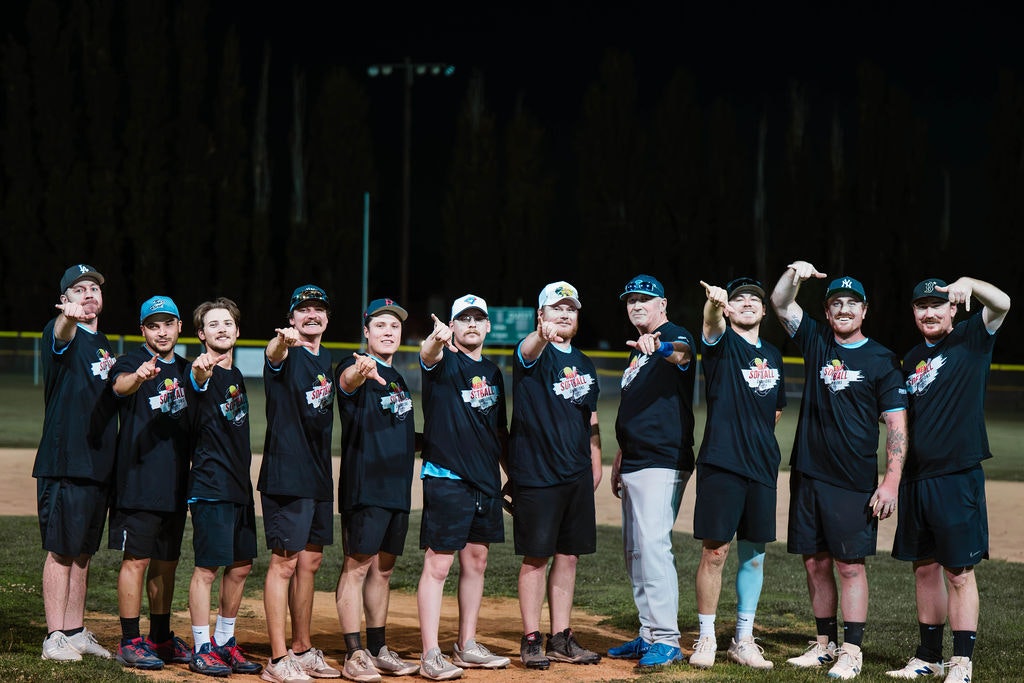 A group of people in matching sports attire pointing forward, standing on a baseball field at night.