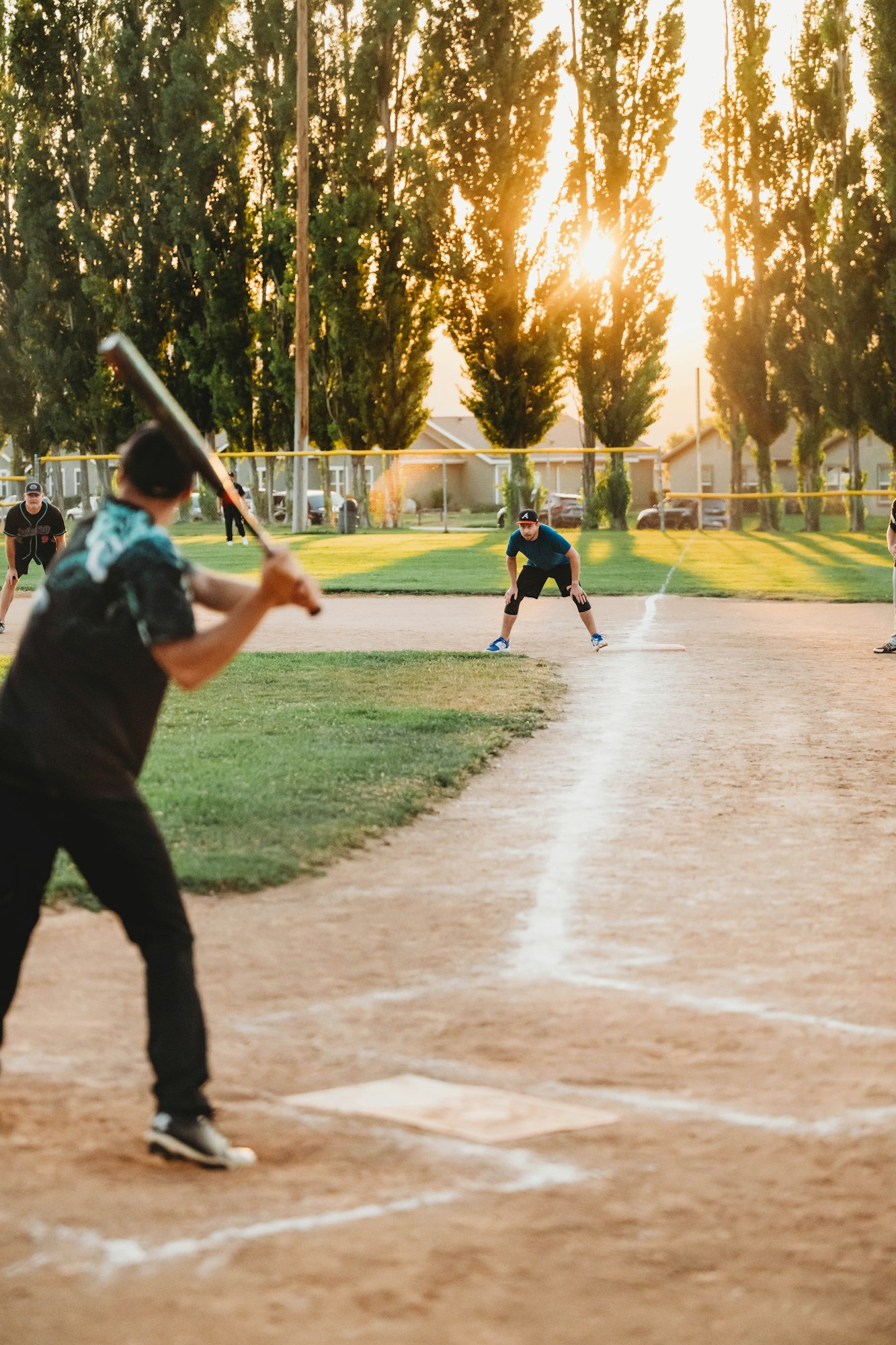 Baseball game with batter ready to hit, infielder poised, and sunset backdrop.