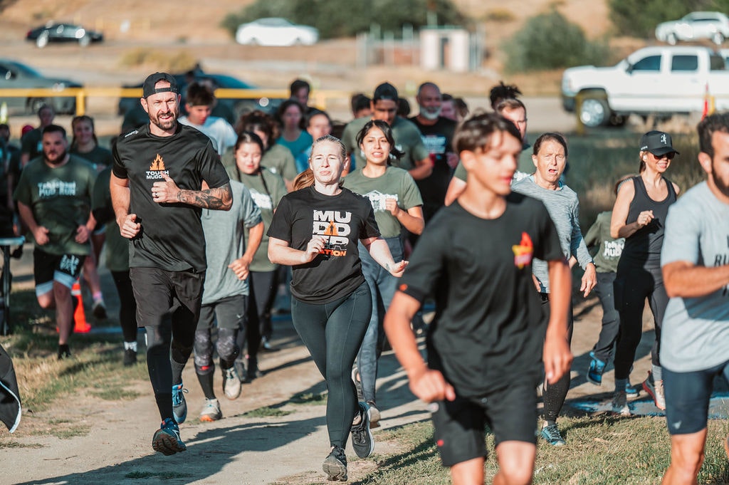 A group of people running outdoors on a sunny day, some wearing "Tough Mudder" shirts.