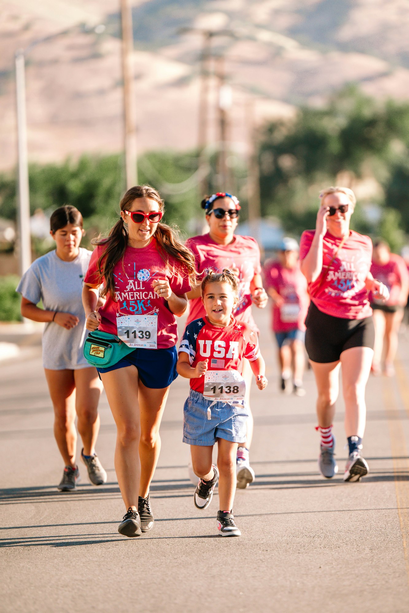 A group of people running in a 5K race wearing matching red shirts, one with "USA" and numbers "1138" and "1139".