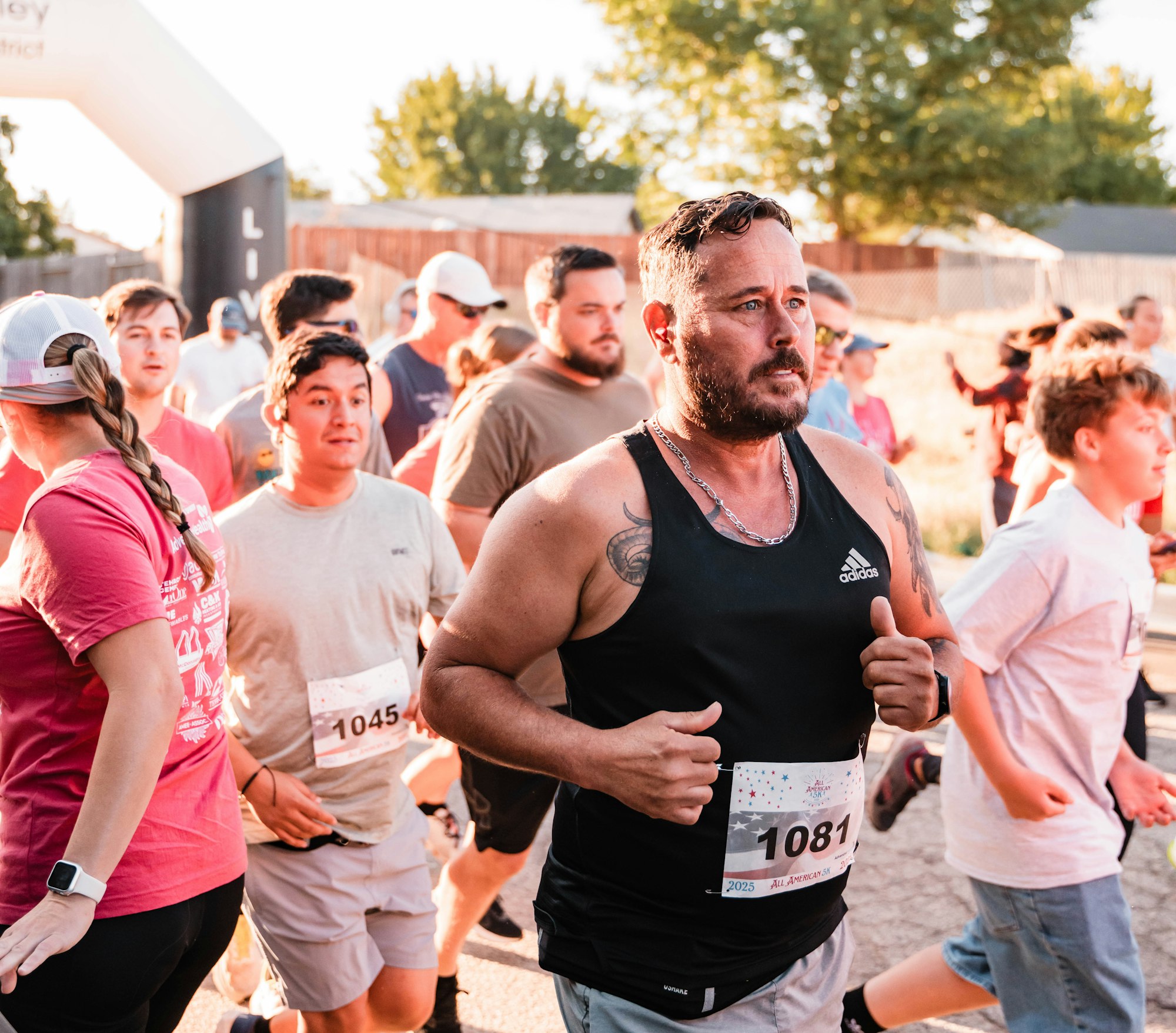A group of people running in a race, wearing numbered bibs, in an outdoor setting.
