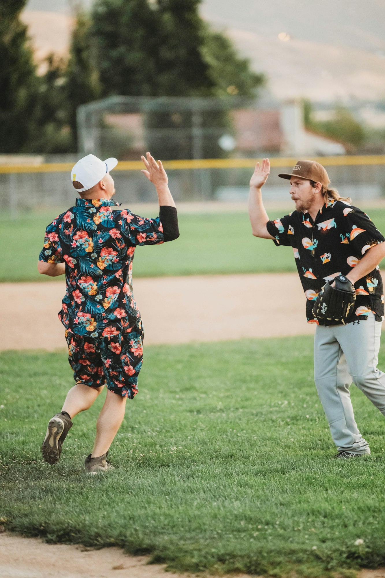 Two people in matching floral outfits high-fiving on a baseball field.