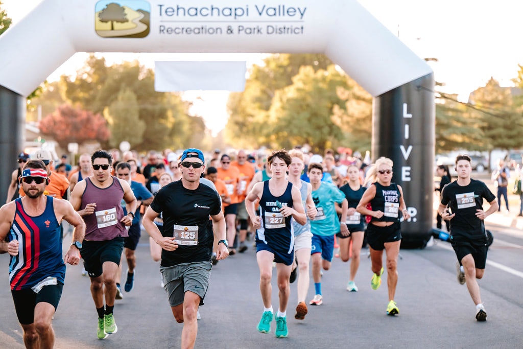 A group of runners participating in a race under an archway labeled "Tehachapi Valley Recreation & Park District."