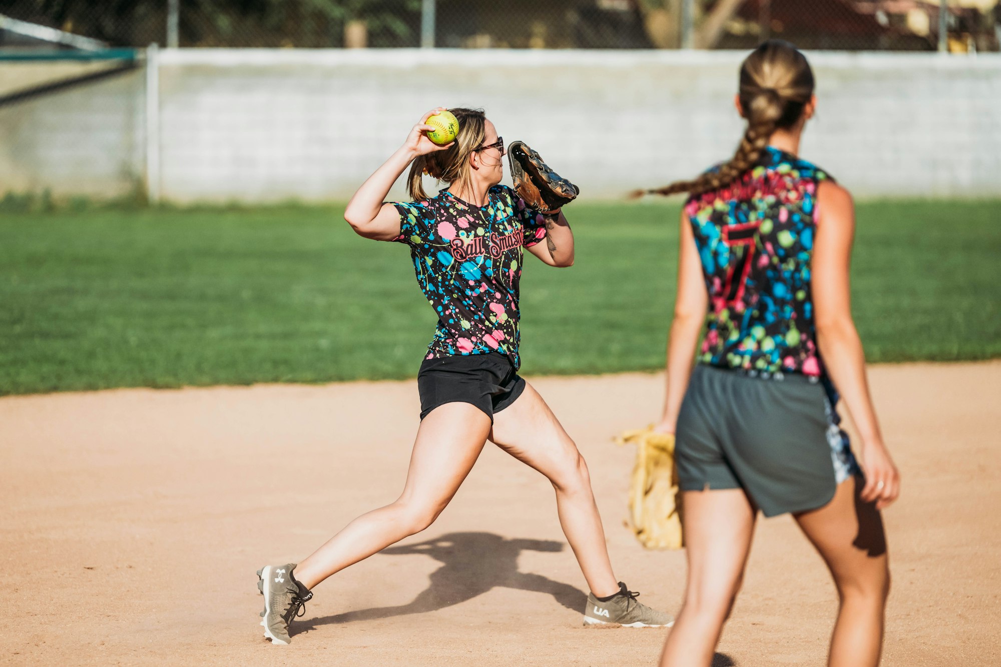 Two softball players in action on a field, one catching a ball.