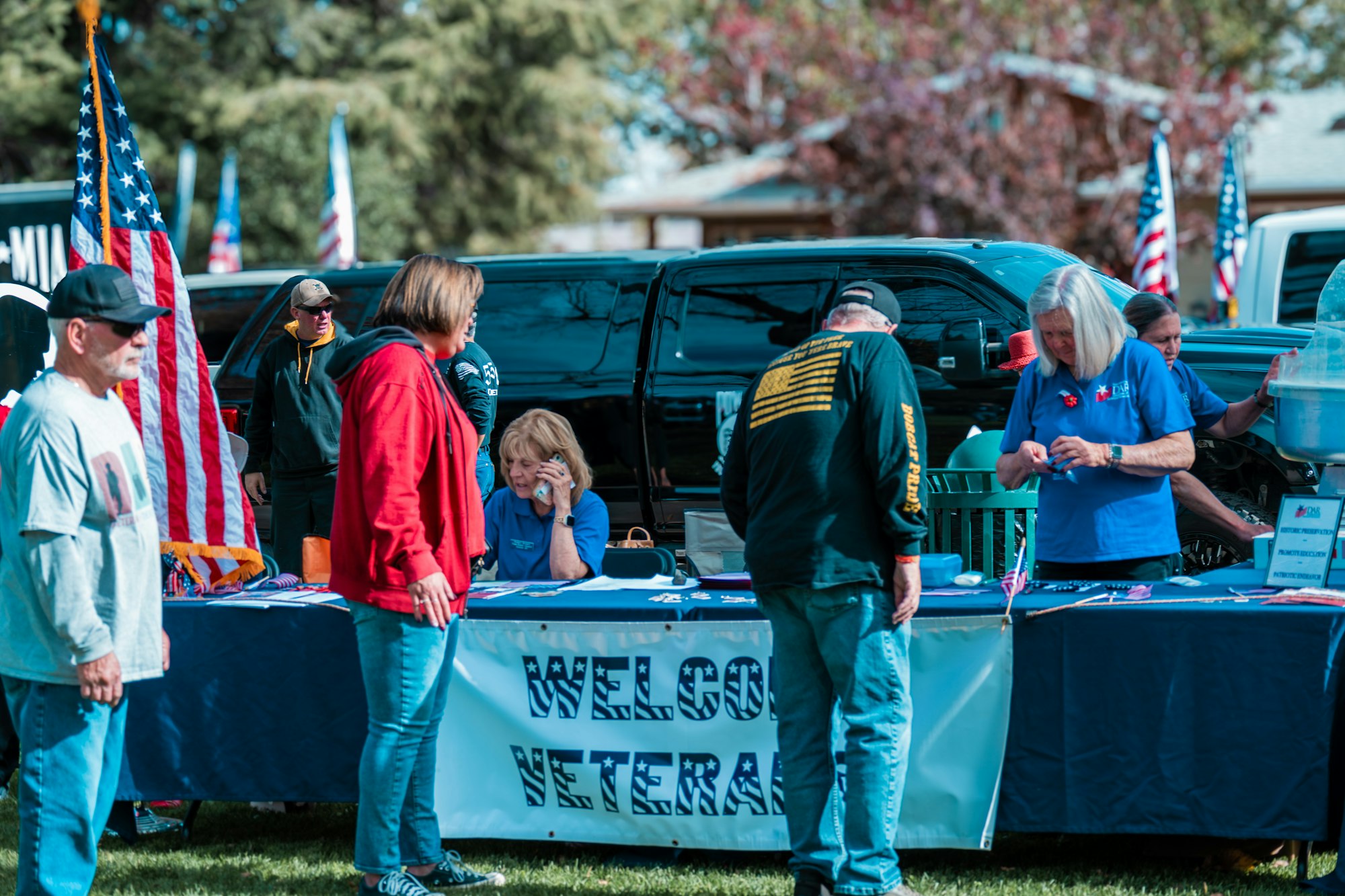 People gathered around a "Welcome Veterans" booth with American flags displayed, possibly at an event honoring veterans.