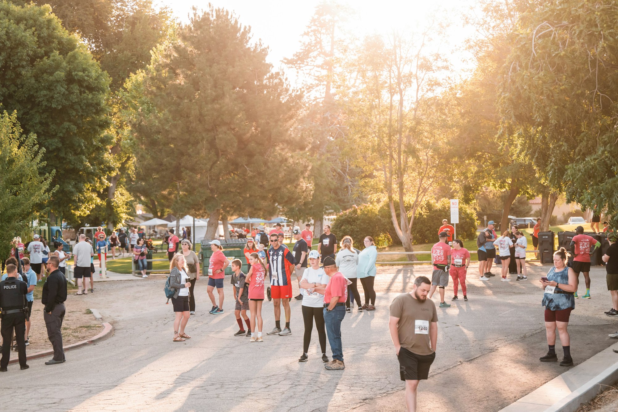 A group of people gathered outdoors, some wearing number bibs, possibly for a running event or festival.