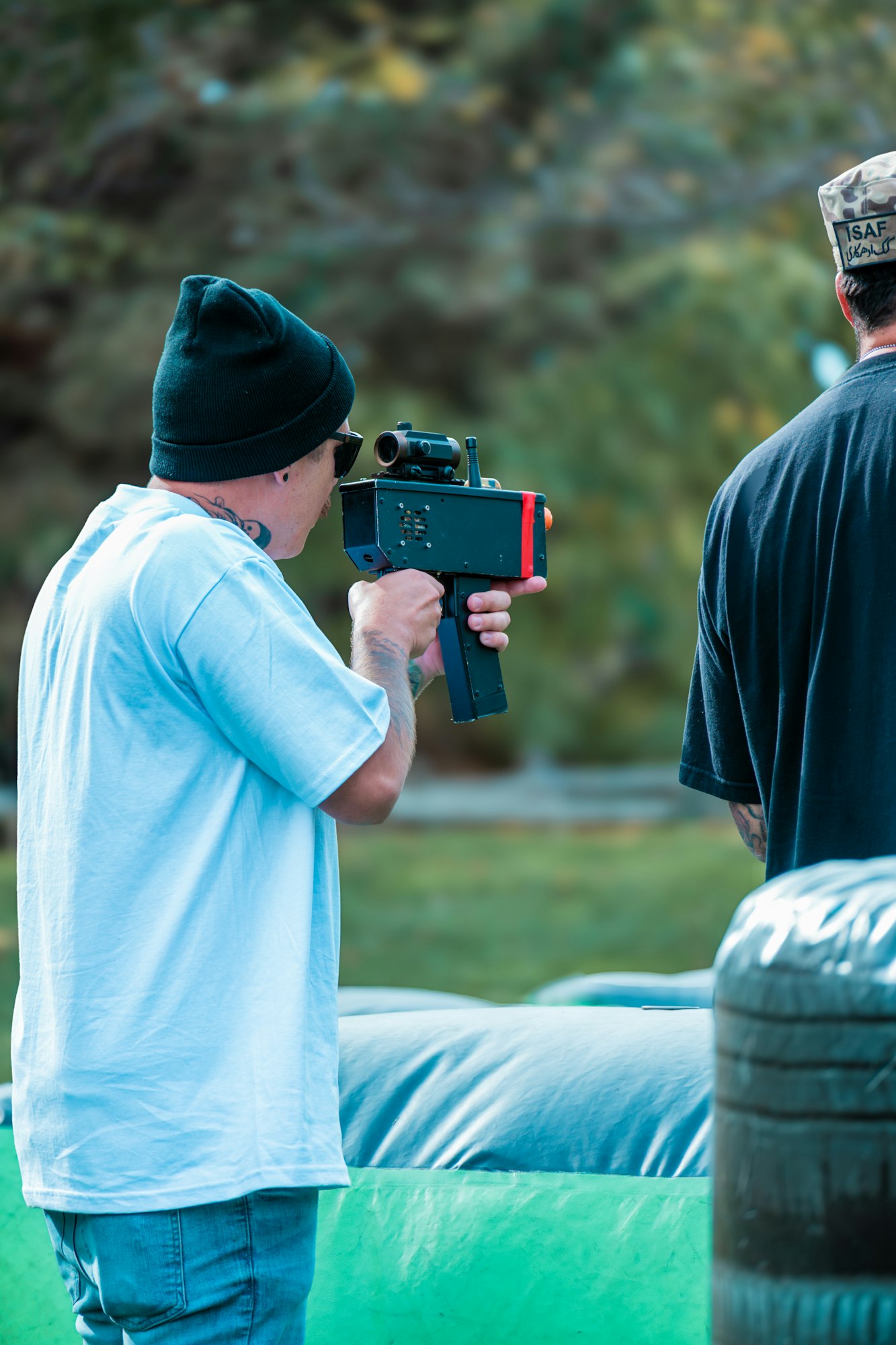Two people playing laser tag; one aiming a laser gun, wearing a beanie and sunglasses.