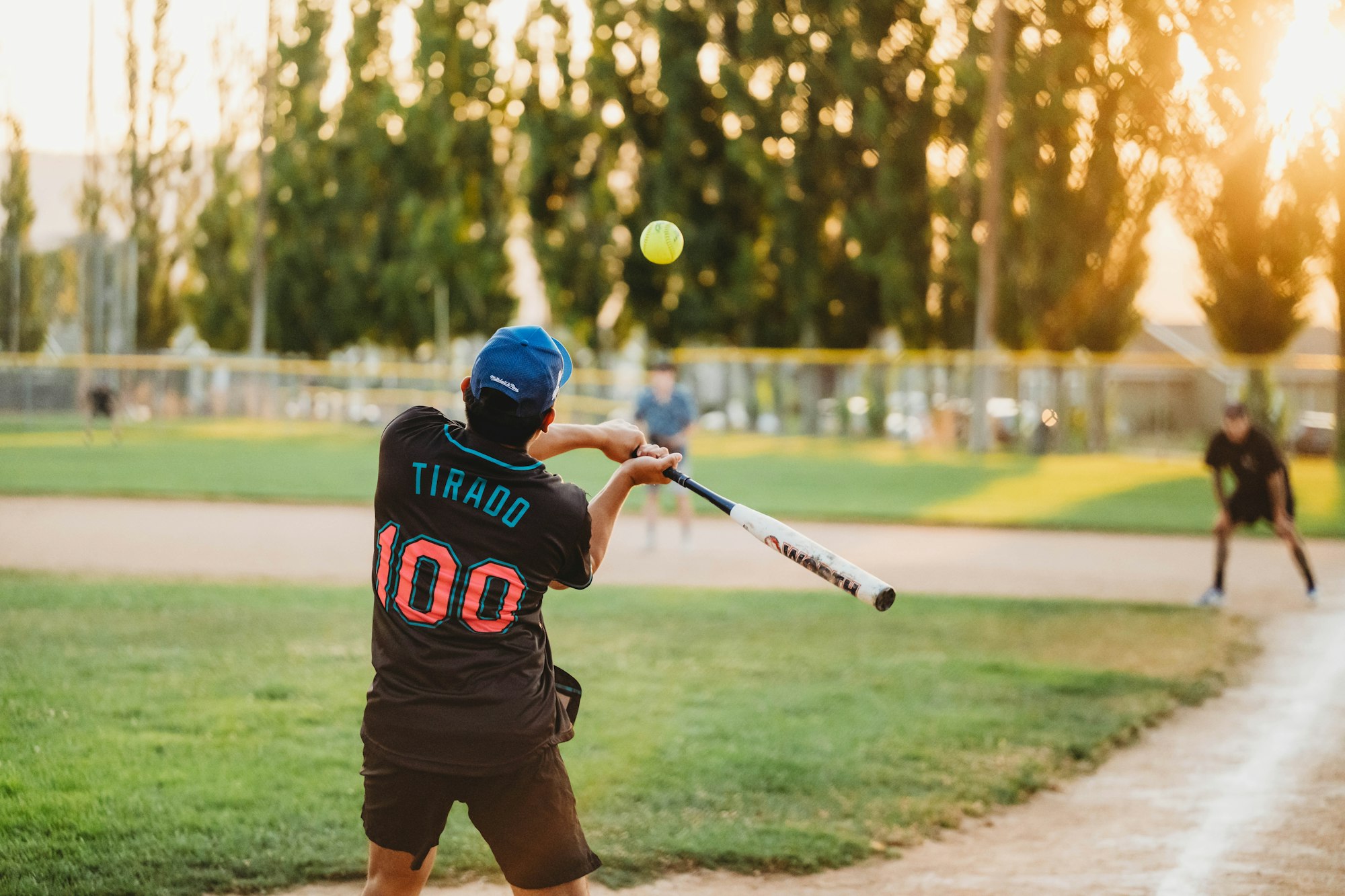 A player is hitting a softball with a bat during a game at sunset.
