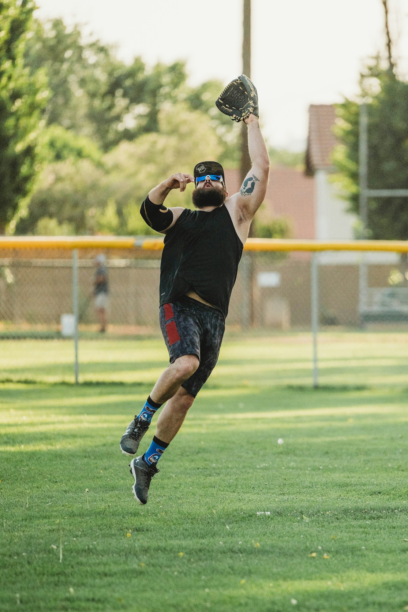 A bearded man in shorts and sports gear jumping to catch a ball with a baseball glove.