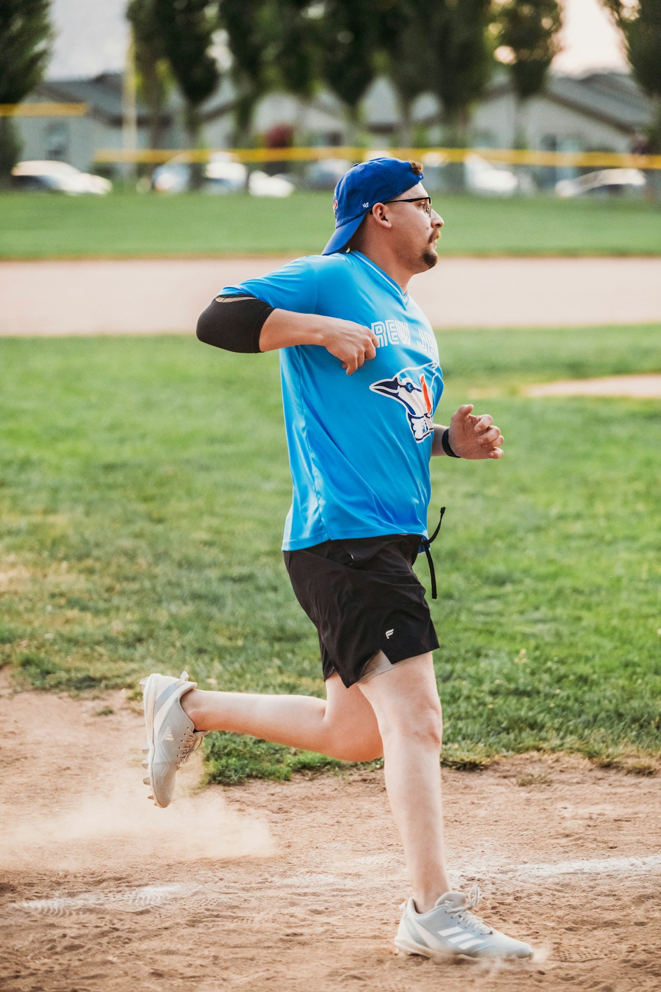 A man in a blue sports jersey and shorts is running on a dusty field.