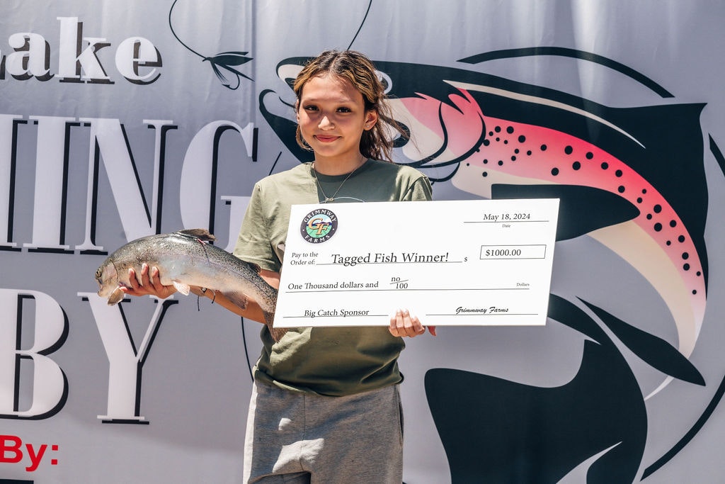 A young winner holding a trout and a $1,000 check for a tagged fish competition.