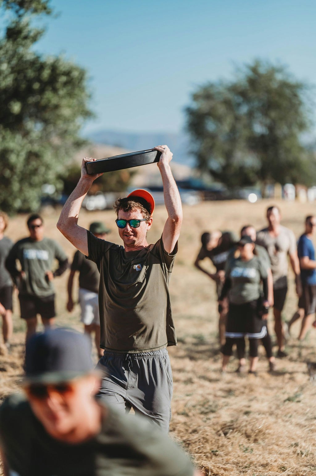 A person outdoors holding an object above their head, with a group in the background.