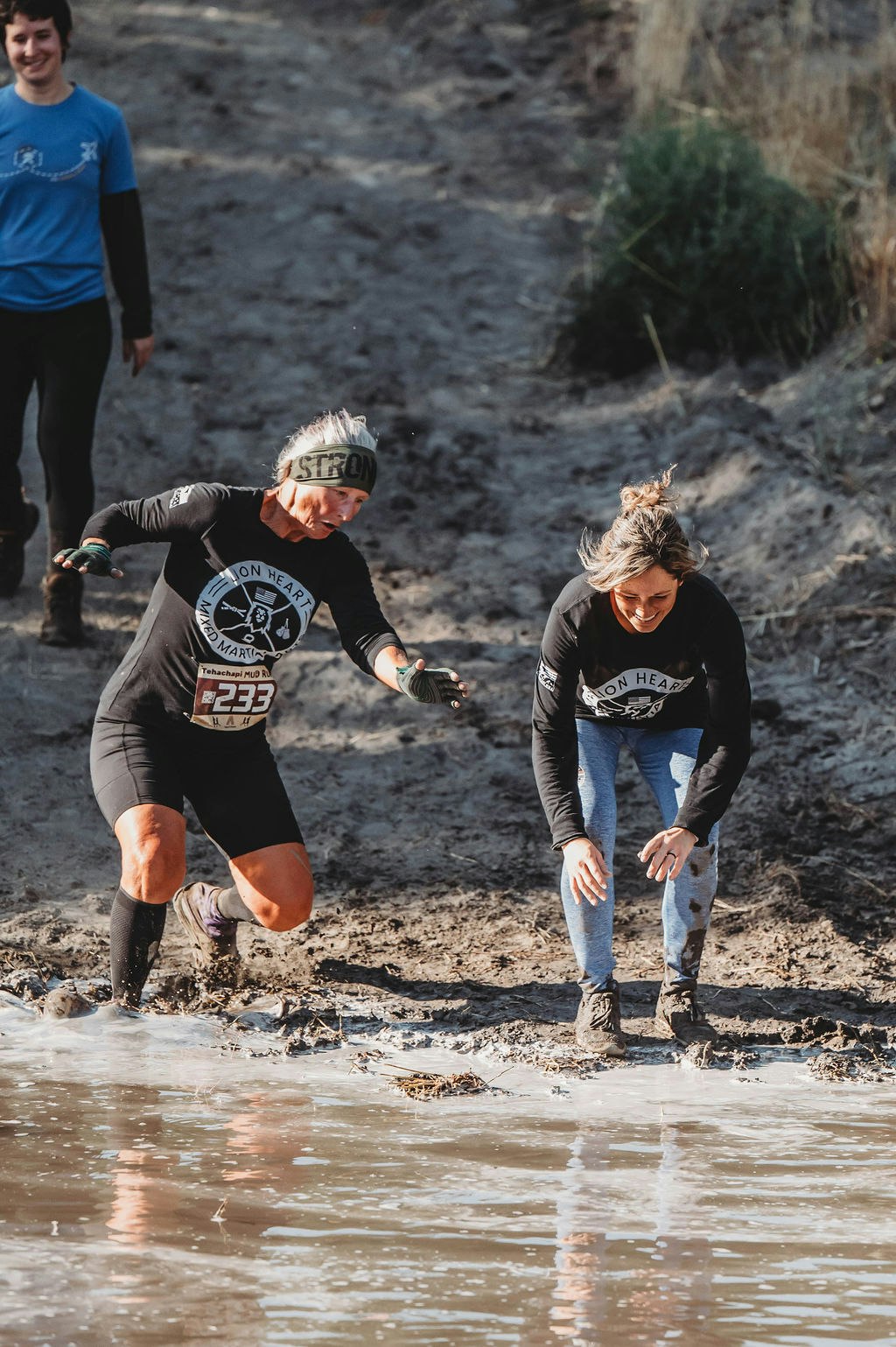 Two people in athletic gear wading through muddy water during an outdoor event.