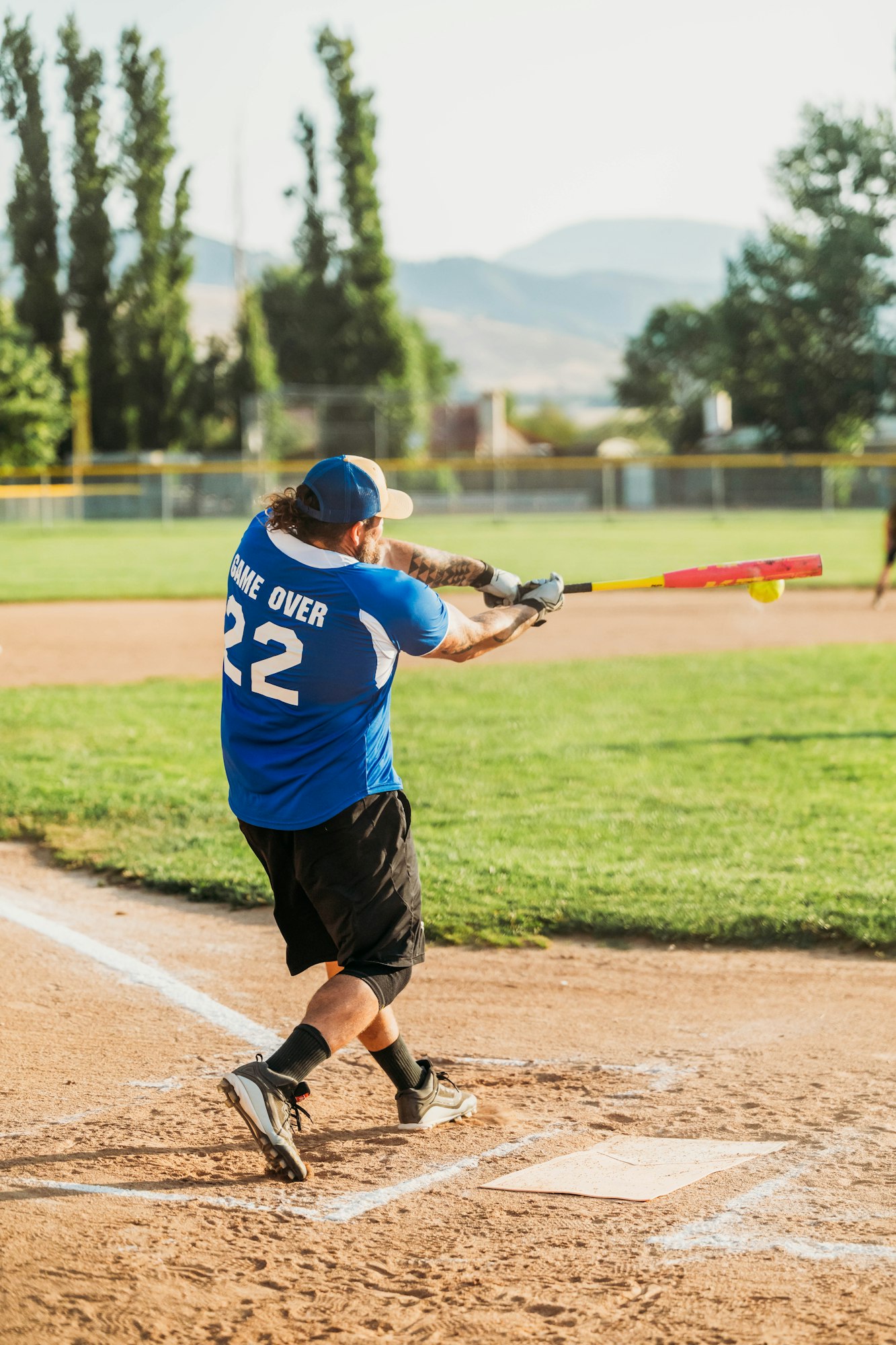 A baseball player mid-swing at home plate, wearing a blue 'GAME OVER' jersey, number 22.