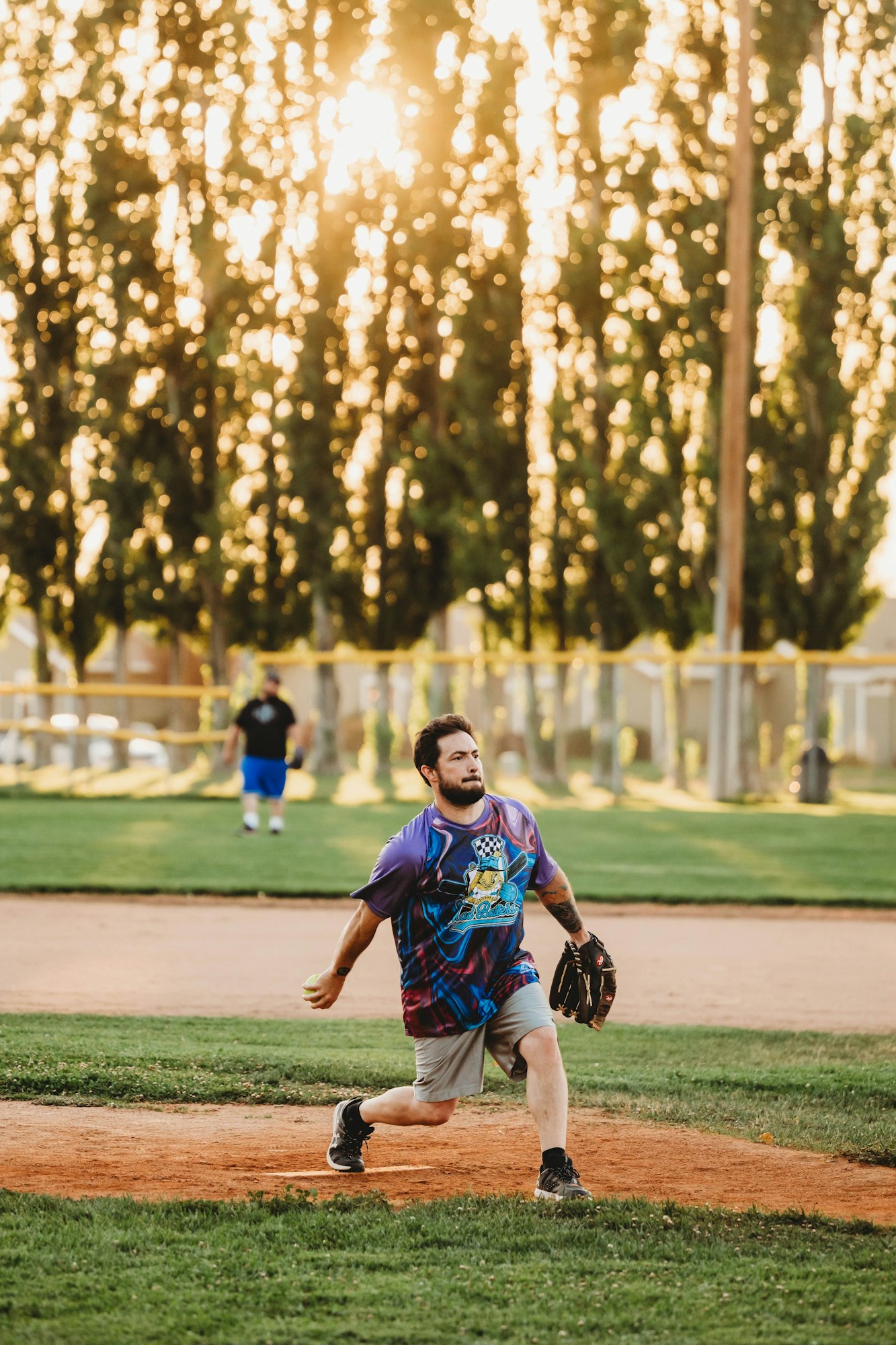 A man pitches a ball on a sunny baseball field.