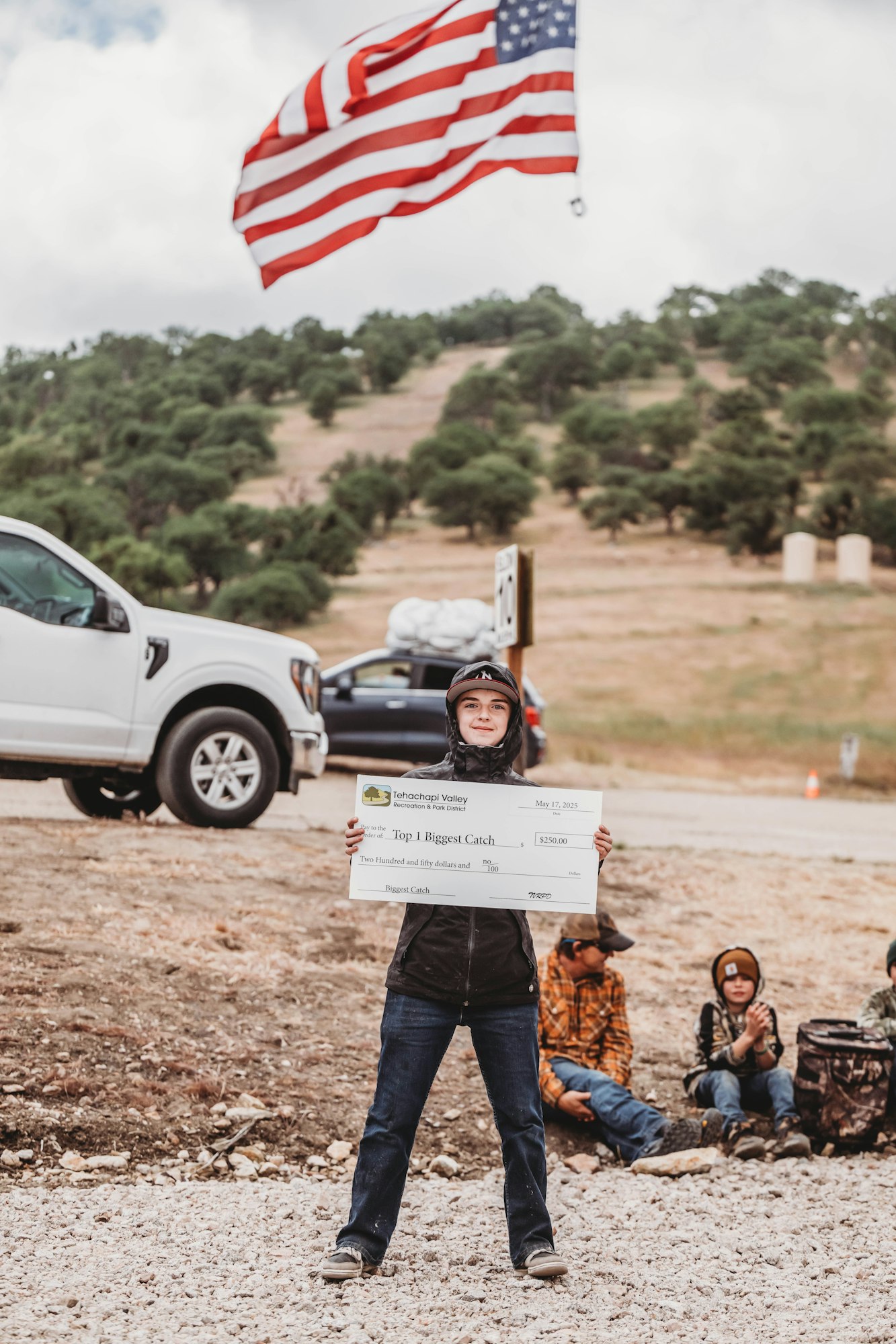 A person holds a big check for "Top 1 Biggest Catch" award. An American flag waves in the background.