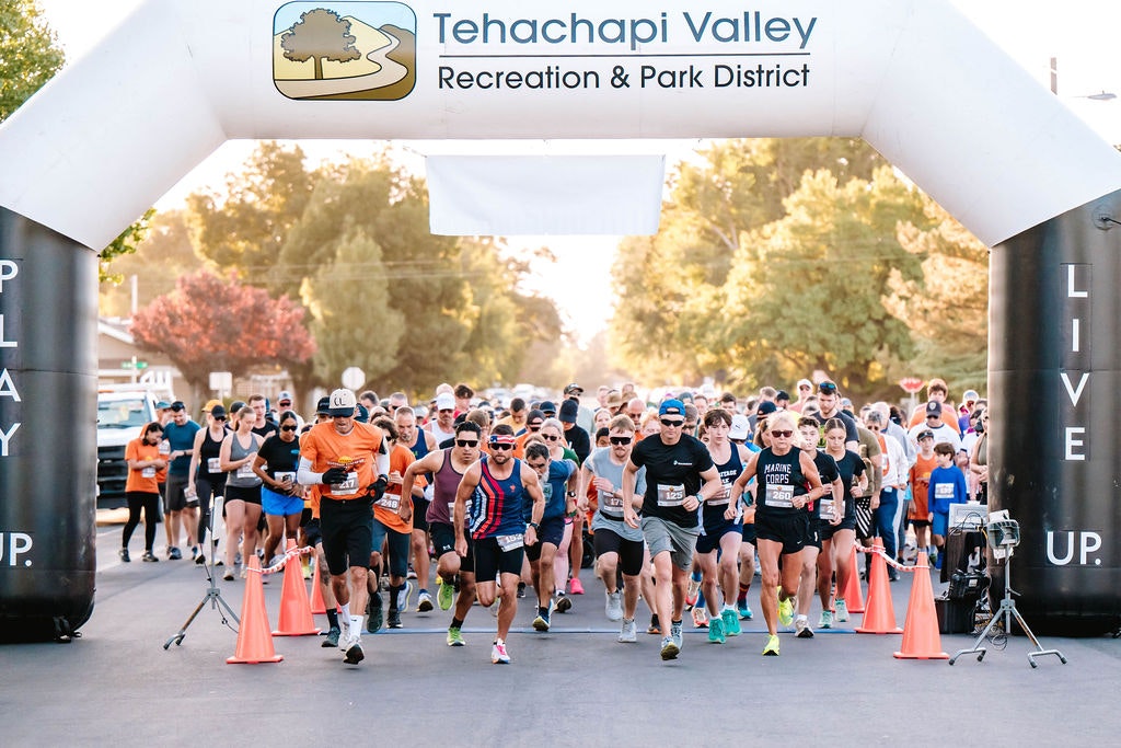 Runners starting a race under an inflatable arch with "Tehachapi Valley Recreation & Park District" banner.
